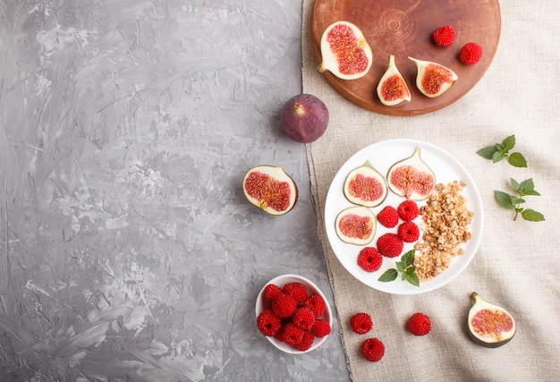 Yogurt con lampone, muesli e fichi in zolla bianca su una priorità bassa concreta grigia