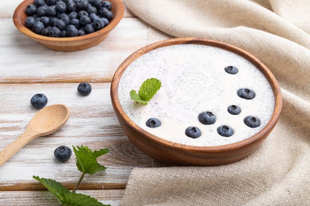 Yogurt con mirtilli in ciotola di legno su superficie di legno bianca e tessuto di lino