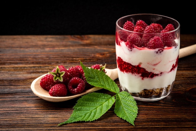 Yogurt con muesli, lamponi e marmellata di lamponi sul tavolo di legno scuro.