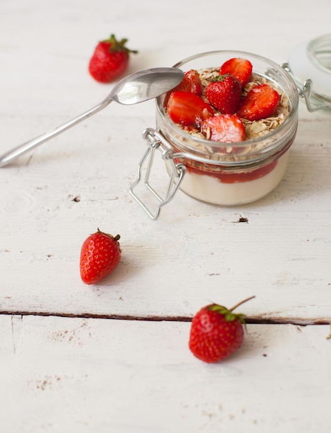 Yogurt dolce con deliziose fragole fresche e cucchiaio sul tavolo di legno bianco