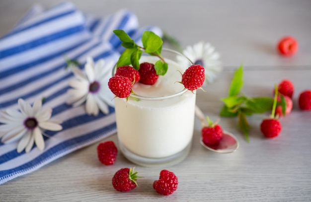 Yogurt domestico cotto dolce con lamponi freschi in un bicchiere su un tavolo di legno leggero