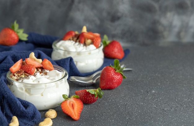 Yogurt greco noci e fragole in vasetti di vetro sul tavolo grigio primo piano spazio copia