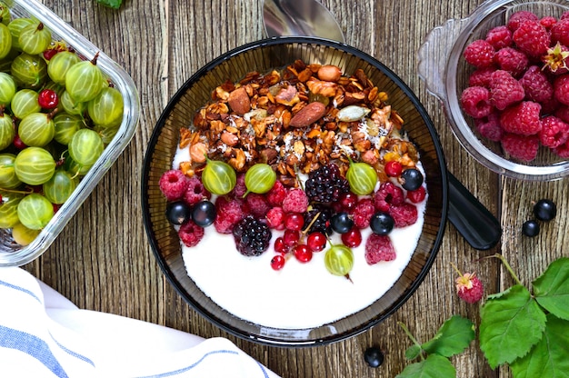 Yogurt, muesli e frutti di bosco freschi in una ciotola su un tavolo di legno