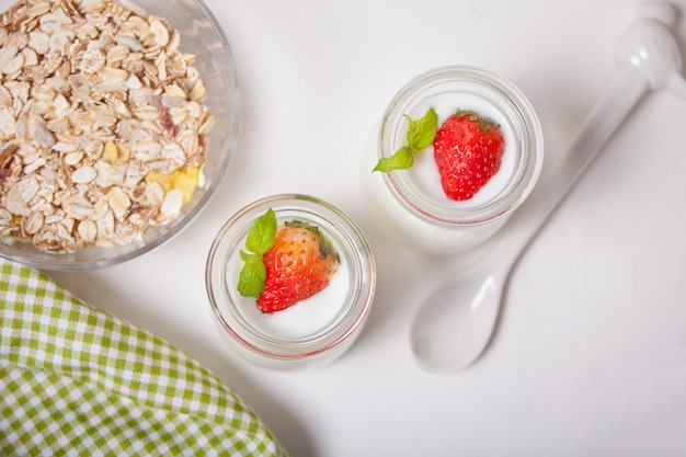 yogurt naturale fatto in casa in un barattolo di vetro con fragole fresche e muesli nelle vicinanze