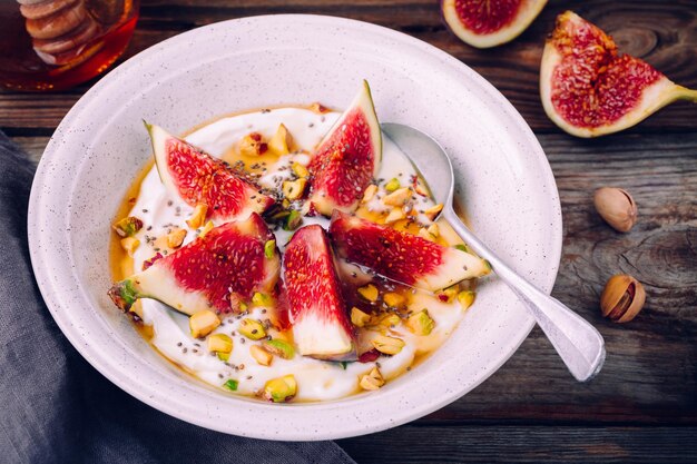 Yogurt naturale per colazione sana con fichi pistacchi semi di chia e miele su fondo di legno