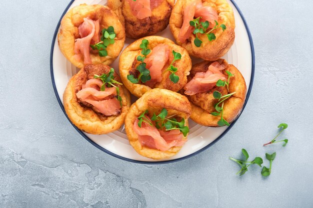 Yorkshire pudding Tradizionale inglese Yorkshire pudding con salmone e ravanello microgreens contorno su piastra bianca e sfondo grigio chiaro tavolo Vista dall'alto