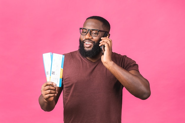 Young African American Black Man Holding Boarding Pass biglietti isolati su sfondo rosa. Utilizzo del telefono cellulare.