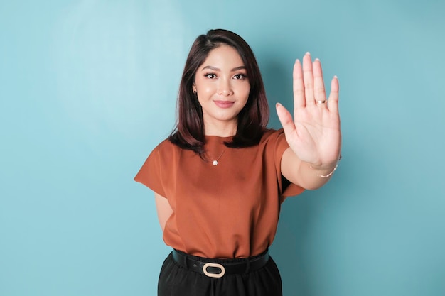 Young Asian woman wearing brown shirt over blue isolated background doing stop sign with palm of the hand