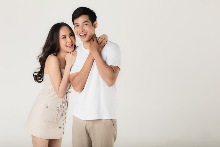 Photo young attractive asian couple, man wearing white t shirt and beige pants, woman wearing beige dress. teasing each other. concept for pre wedding photography.