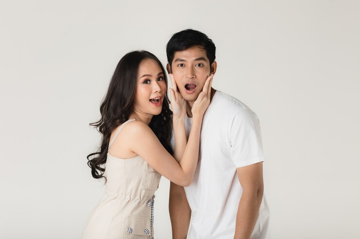 Photo young attractive asian couple, man wearing white t shirt and beige pants, woman wearing beige dress. teasing each other. concept for pre wedding photography.