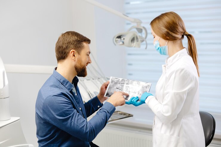 Young attractive man visiting dentist sitting in dental chair at modern light clinic Young woman dentist holding x ray image