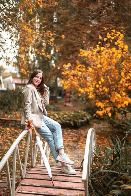 Young beautiful girl in jeans and a casual jacket in an autumn park stand on the bridge golden autumn