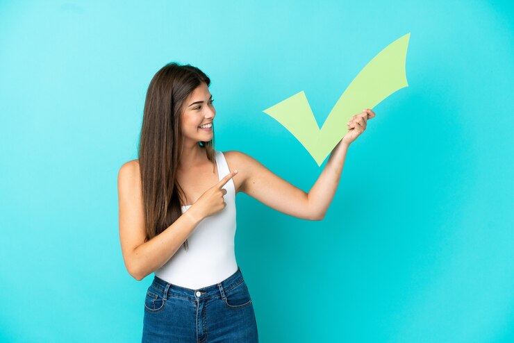 Photo young brazilian woman isolated on blue background holding a check icon and pointing it