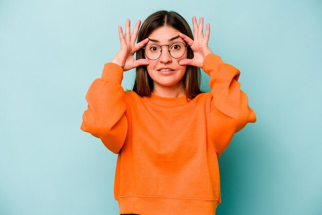 Young caucasian woman isolated on blue background keeping eyes opened to find a success opportunity