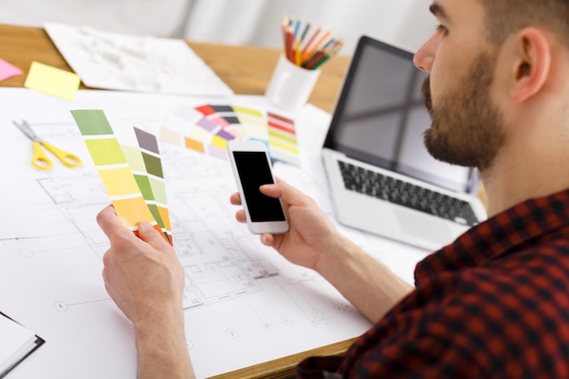 young designer in casual working with color palette and smartphone in modern workplace interior, copy space