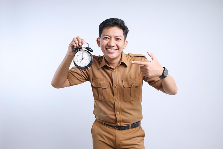 Photo young indonesian government worker man in brown khaki uniform pointing at alarm clock that he hold