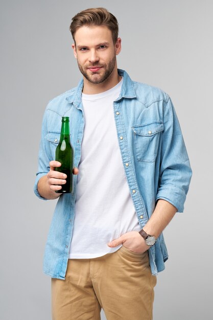 Young Man holding indossa jeans shirt Bottiglia di birra in piedi