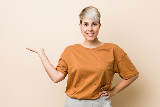 Young plus size donna con i capelli corti che mostra una su un palmo e che tiene un'altra mano sulla vita.