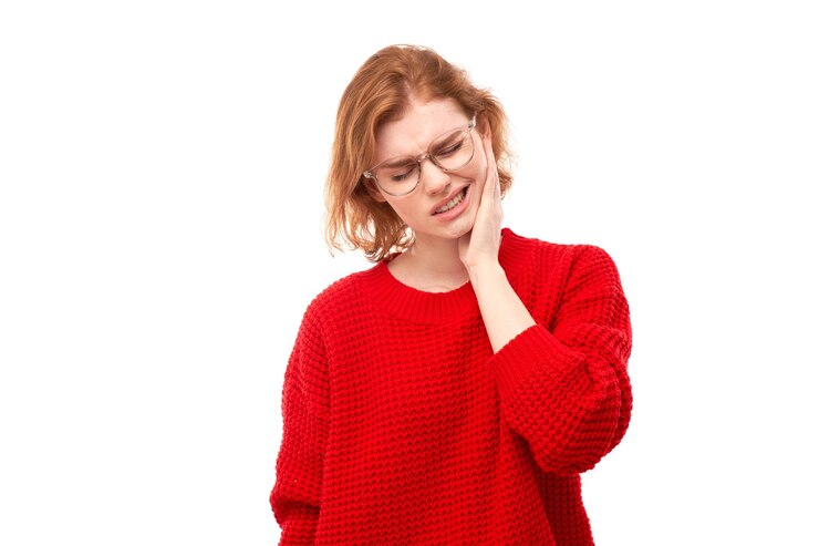 Young redhead woman with suffering face expression holds cheek with hand touching mouth with palm isolated on white background Toothache dental pain concept