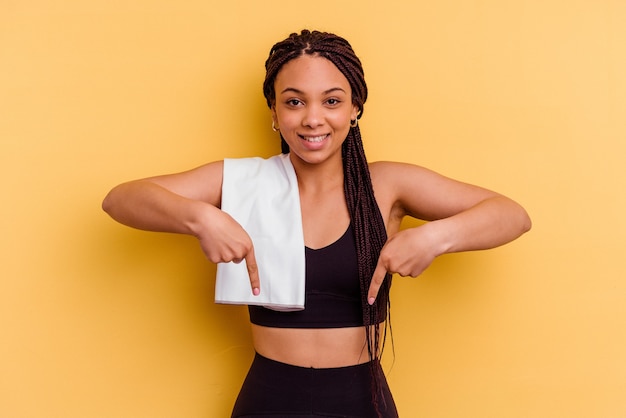 Young sport donna afro-americana che tiene un asciugamano isolato sulla parete gialla punta verso il basso con le dita, sensazione positiva.
