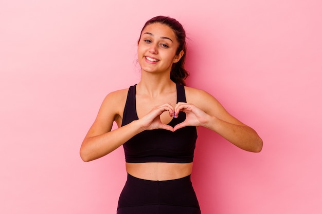 Young sport donna indiana isolata su sfondo rosa sorridente e mostrando una forma di cuore con le mani.