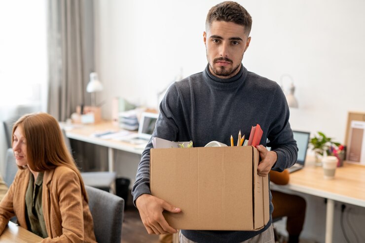 Photo young unhappy employee holding box with office supplies
