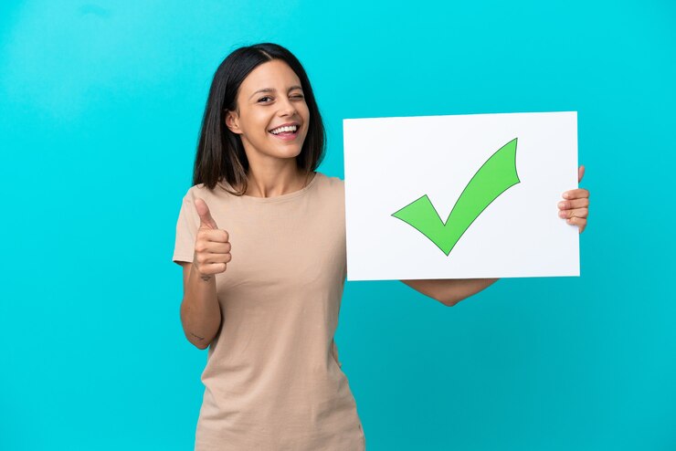 Photo young woman over isolated background holding a placard with text green check mark icon and pointing to the front