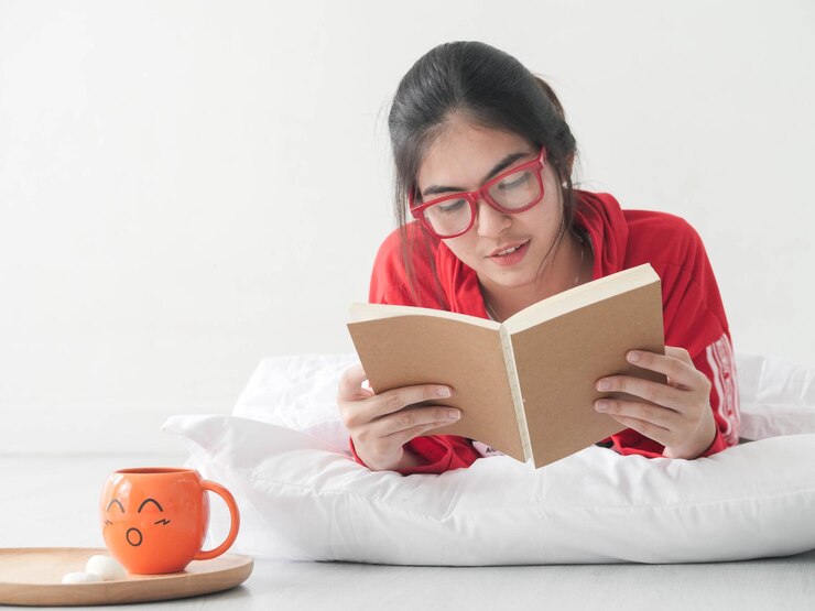 Photo young woman reading book while lying on floor against wall