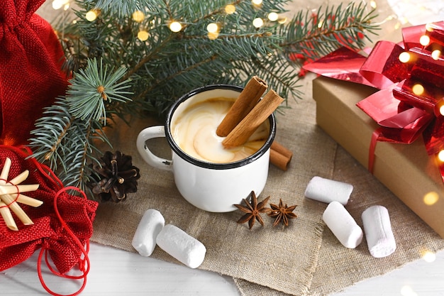 Zabaione con anice alla cannella e noce moscata in una tazza bianca vicino ai rami di un albero di Natale