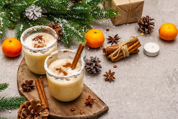 Zabaione con cannella e noce moscata per Natale e vacanze invernali. Bevanda fatta in casa in bicchieri con bordo speziato. Mandarini, candele, regali.