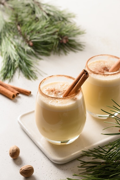 Zabaione di Natale con cannella sulla tavola bianca decorata rami sempreverdi.