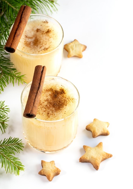 Zabaione tradizionale della bevanda di Natale con la cannella in due bicchieri Biscotti di Natale stelle su bianco