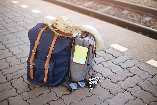 Zaino con cappello, mappa, occhiali da sole, auricolare e smartphone nella stazione ferroviaria