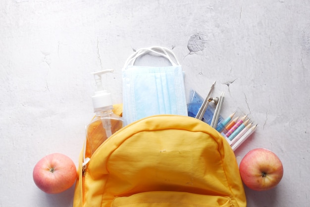 Zaino da scuola per studenti con disinfettante e maschera facciale sul tavolo