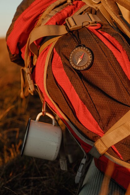 Zaino da trekking rosso con bussola magnetica e tazza da viaggio in metallo a terra nella natura autunnale al tramonto