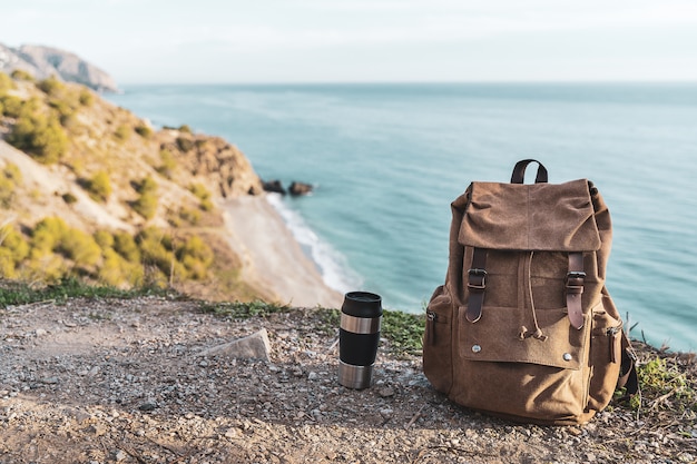 Zaino e thermos di caffè con la costa in background. Concetto di esplorazione e avventure