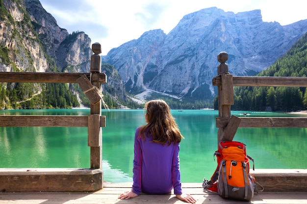 Zaino in spalla ragazza seduta su un molo e guardando il lago di Braies, Dolomiti Italia