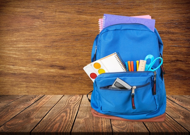 Zaino scuola classico con materiale scolastico colorato e libri sulla scrivania.