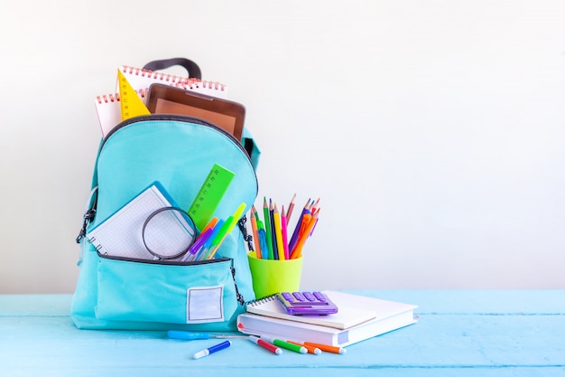 Zaino scuola turchese pieno con elementi decorativi sul tavolo.