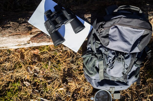 Zaino turistico, cappello, binocolo e una mappa su un tronco nella foresta