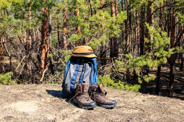 Zaino turistico, scarpe da trekking e cappello sulla radura in pineta. Concetto di escursione