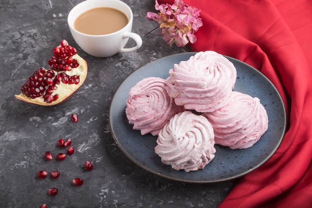 Zephyr o marshmallow fatti in casa rosa melograno con una tazza di caffè su una superficie di cemento nero con tessuto rosso