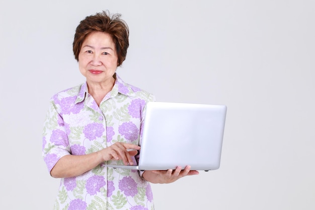 Zia asiatica anziana come insegnante anziana che gioca a un laptop aziendale per spiegare la promozione della vendita e il messaggio pubblicitario pubblico del dispositivo elettronico. La nonna presenta le informazioni sulla tecnologia per l'adulto in pensione.