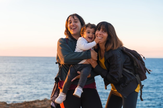 Zia del bambino e madre che abbracciano con lui bambino sulla costa in riva al mare al tramonto