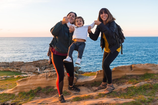 Zia del bambino e madre che giocano con lui sulla costa in riva al mare al tramonto