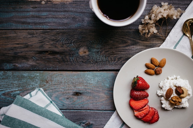 Zolla con la ricotta, le fragole e le noci, una tazza di caffè e gli asciugamani sulla tavola di legno, alimento sano, prima colazione