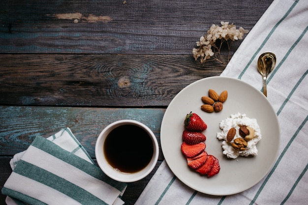 Zolla con la ricotta, le fragole e le noci, una tazza di caffè e gli asciugamani sulla tavola di legno, alimento sano, prima colazione