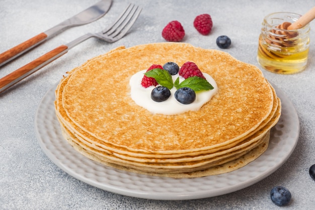 Zolla dei pancake sottili deliziosi con le bacche sulla tabella grigia