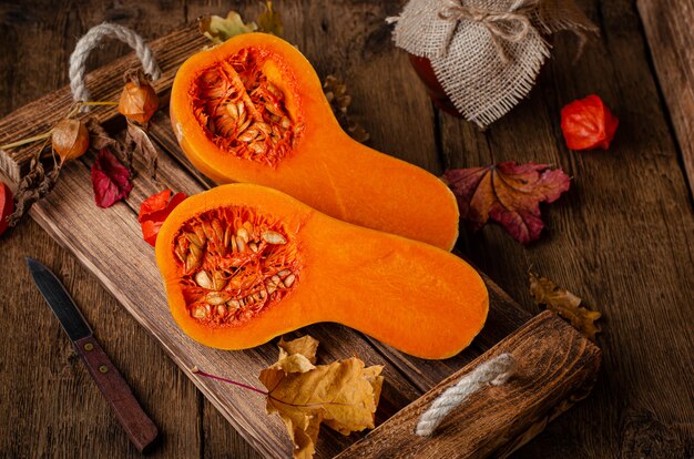 Zucca arancio divisa in due sul vassoio di legno rustico. Dieta sana e natura morta rurale