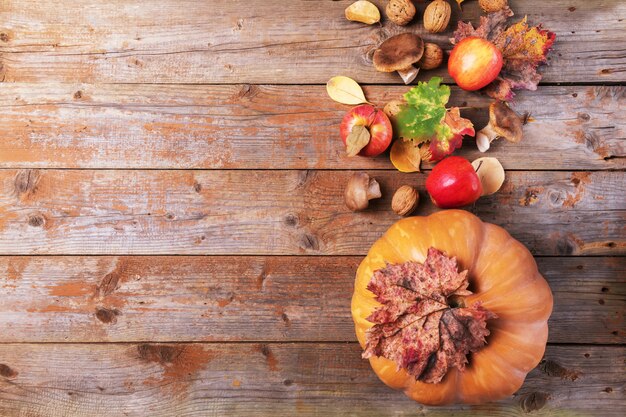 Zucca arancione con funghi cardoncelli, mele, noci e foglie colorate su vecchie tavole di legno rustici. Sfondo autunno giorno del ringraziamento